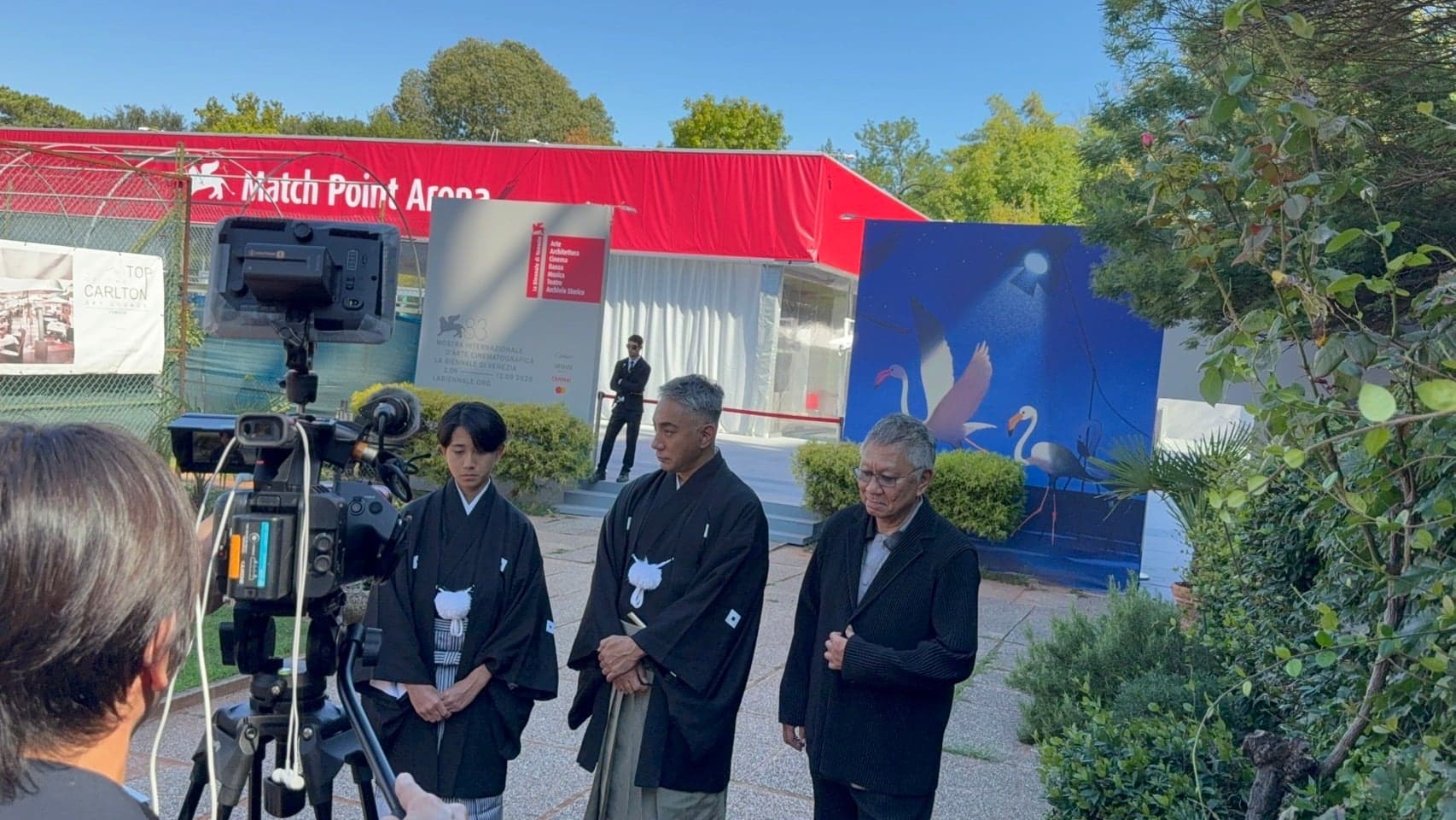 映画祭会場での取材。黒紋付姿の三人がカメラの前に立つ